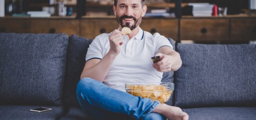 smiling man watching tv and eating chips at home