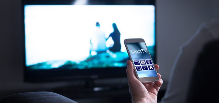 man watching television and using tv remote application on mobile