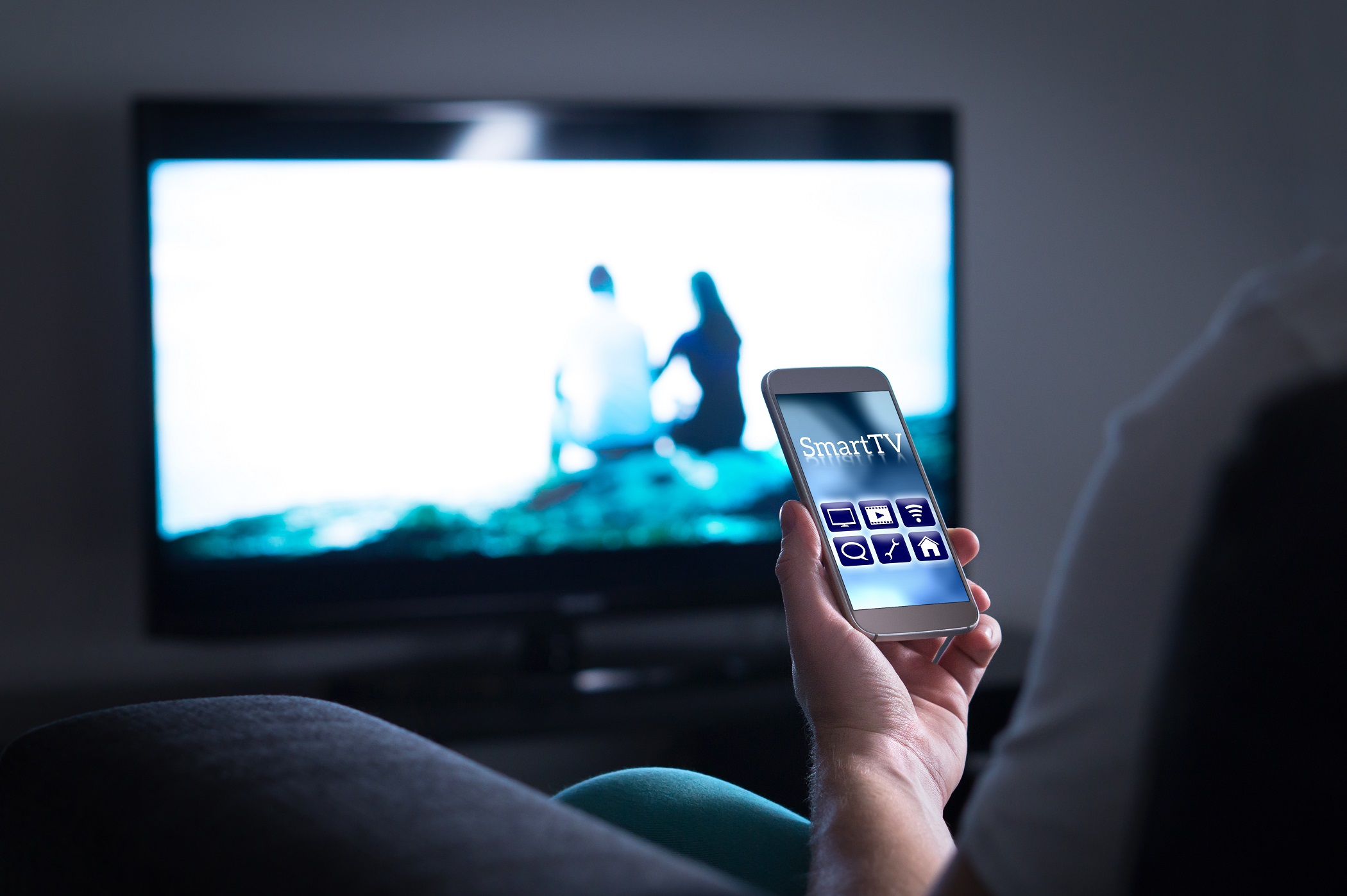 man watching television and using tv remote application on mobile