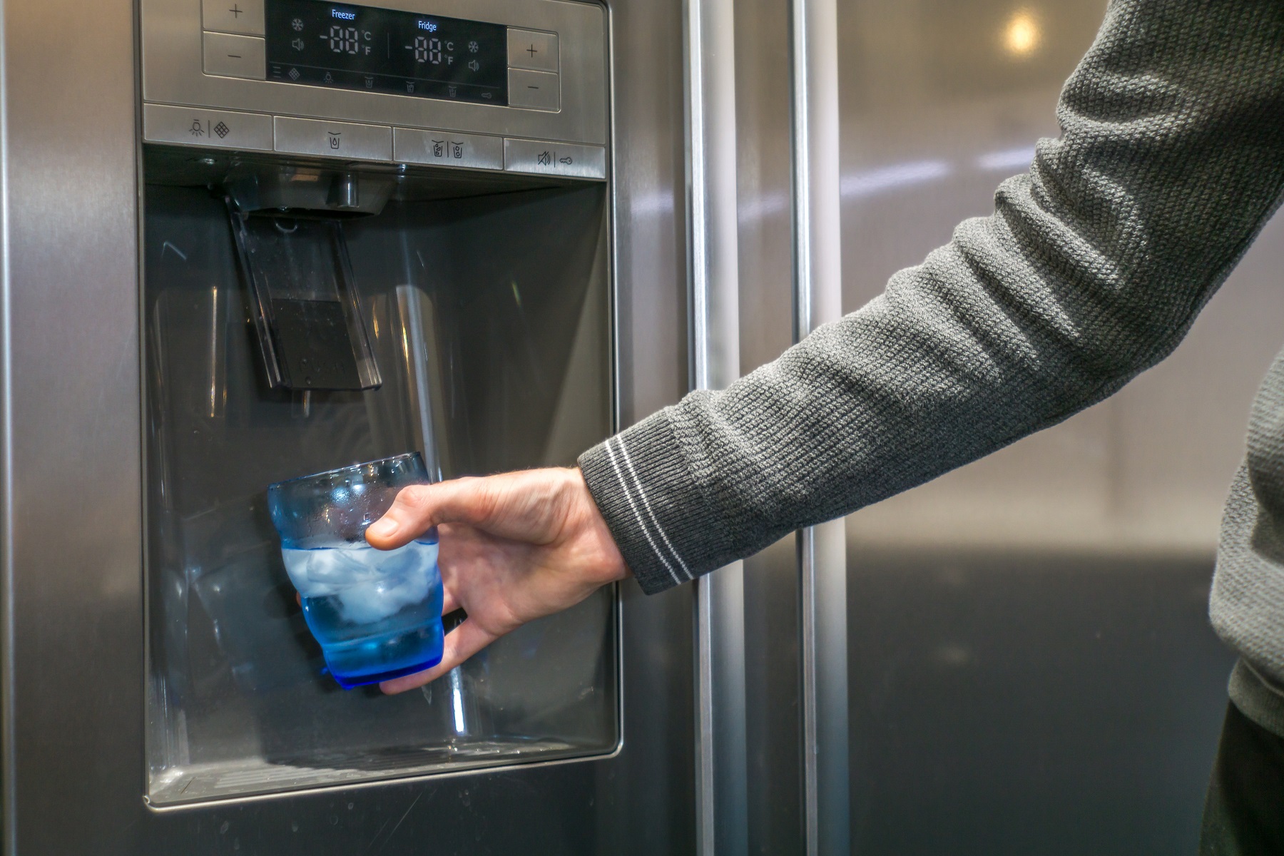 Male hand is pouring water and ice cubes from dispenser of fridge