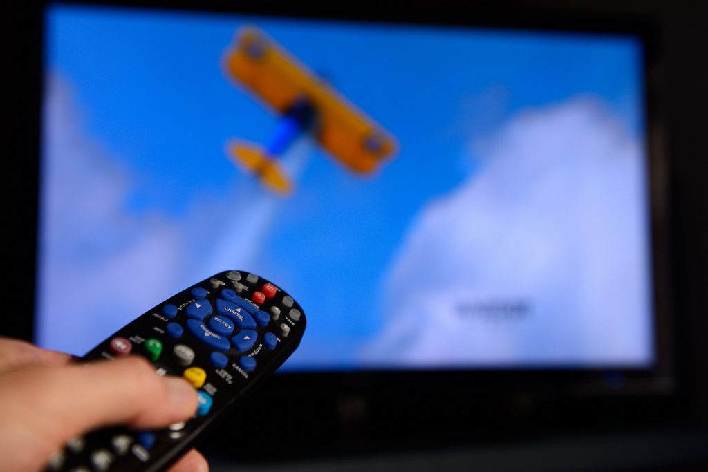 Man pointing a universal remote control towards a television screen