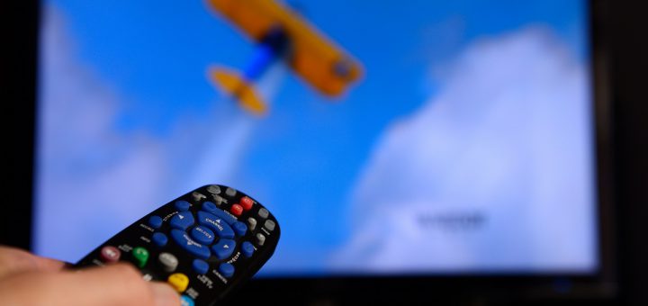 Man pointing a universal remote control towards a television screen