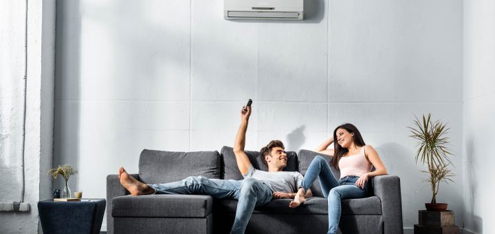 handsome boyfriend switching on air conditioner and looking at smiling girlfriend