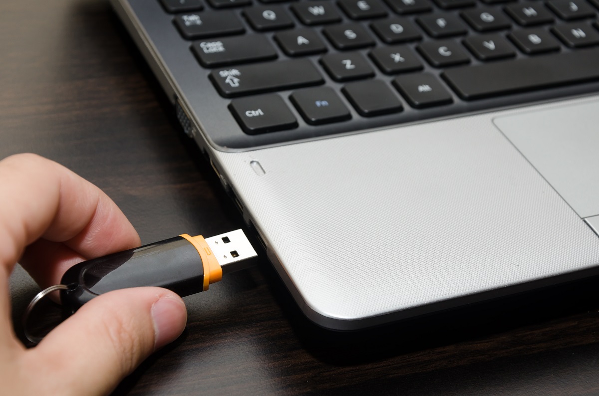 hand with usb flash drive inserting it into laptop computer closeup