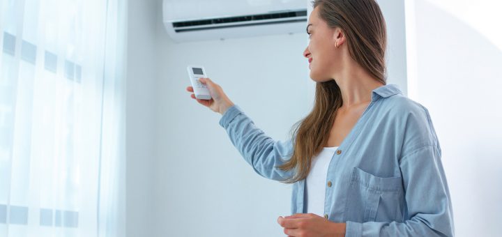 Young woman adjusts the temperature of the air conditioner using the remote control