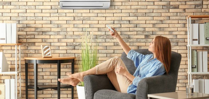 Young woman switching on air conditioner while sitting in armchair