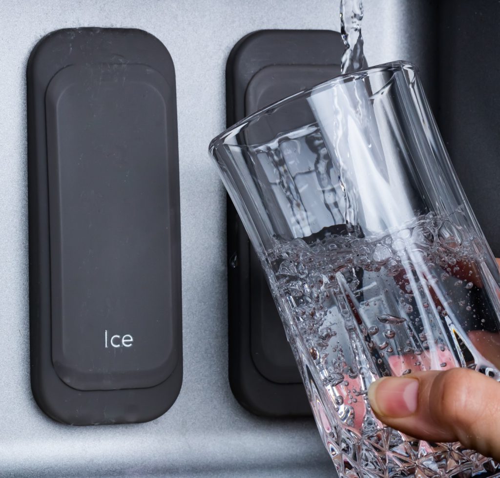 hand with a glass of water against a water dispenser in the fridge