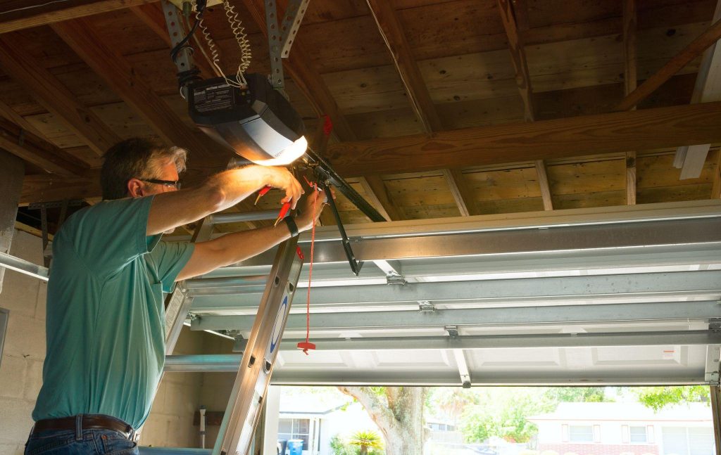 Professional automatic garage door opener repair service technician man working on a ladder at a home residential