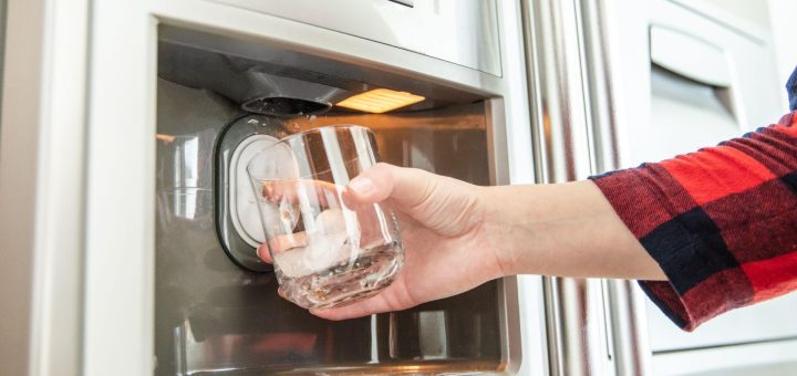 Woman's hand holds glass and uses refrigerator to make fresh clean ice cubes.