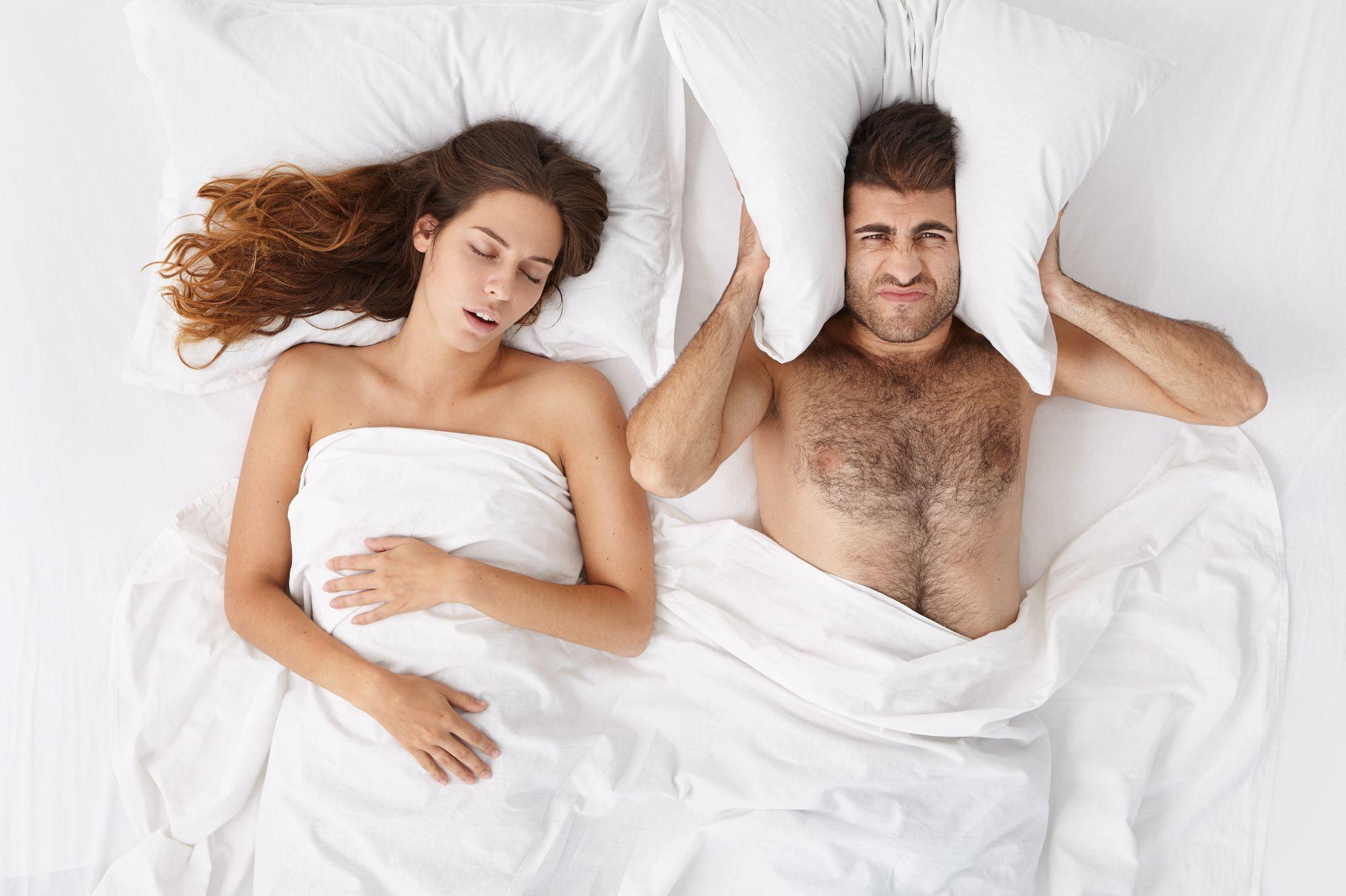 a couple laying in bed while the woman snores and the man is upset he cannot sleep